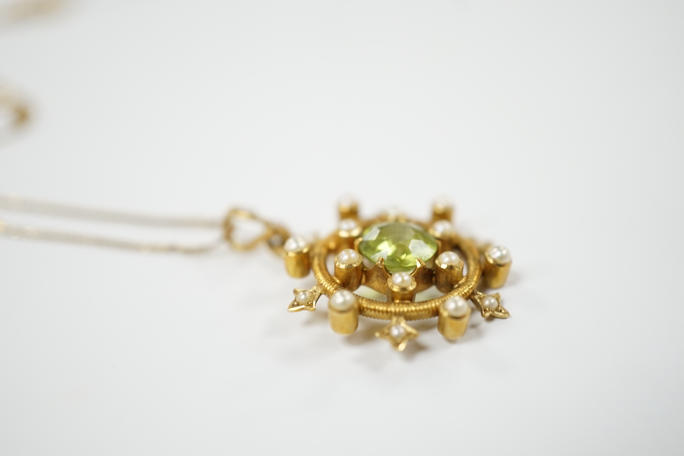 An Edwardian yellow metal, peridot and seed pearl cluster set 'wheel' pendant, overall 30mm, on a later 14k chain, gross weight 5.2 grams.